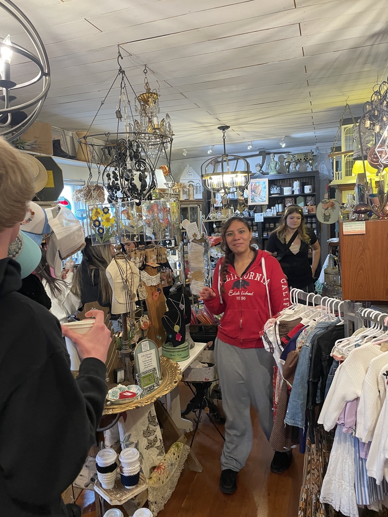 A person in a red jacket talks in a shop with wooden floors, a ceiling, and hanging clothes.