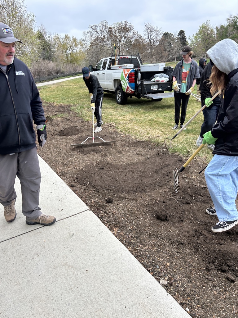 People digging soil outdoors. One person holds a shovel. A white pickup truck is parked in the background.