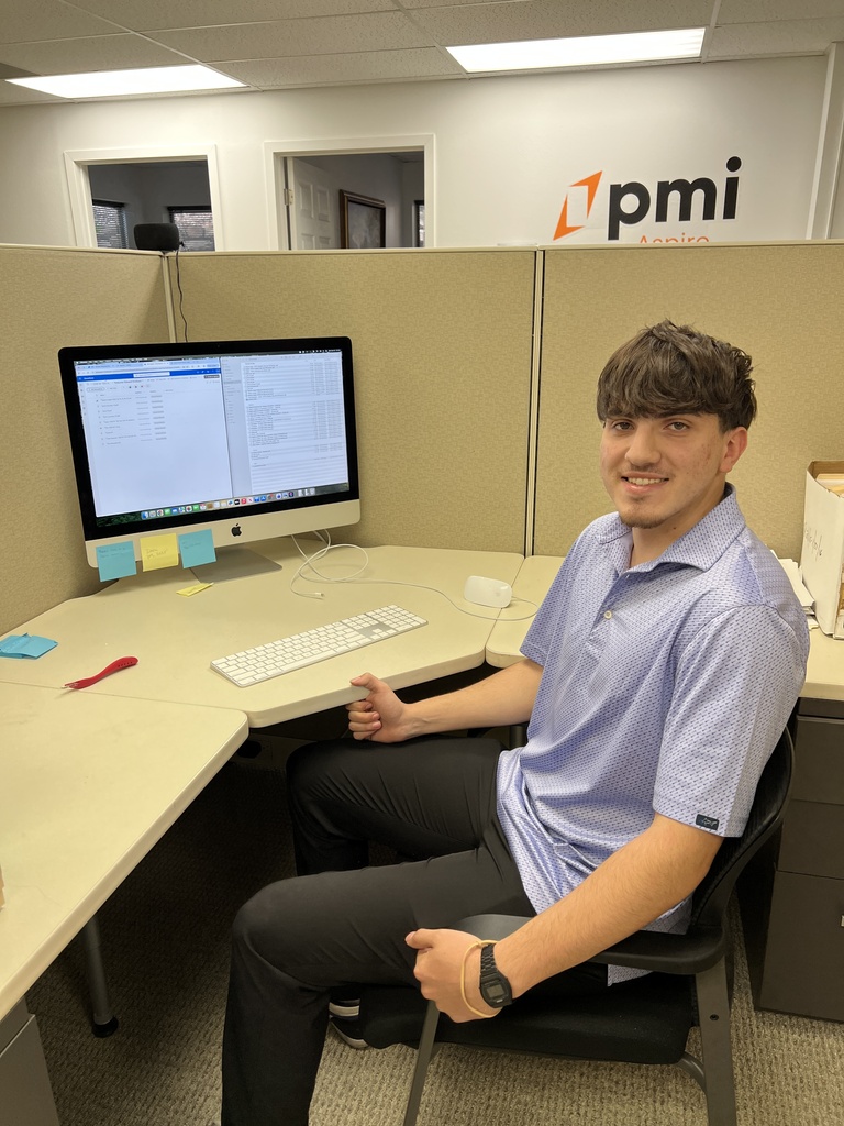 Person in an office cubicle with a computer, keyboard, mouse, sticky notes, and a red pen.