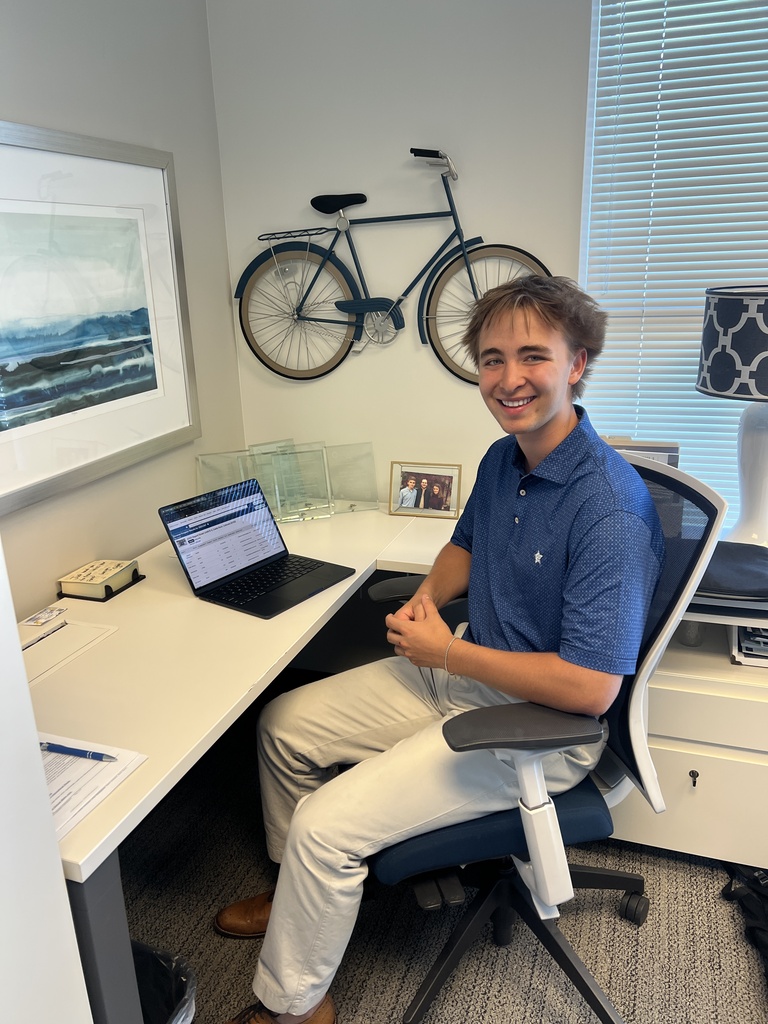 Man sitting at a desk, smiling. A framed picture, bicycle, and lamp on a desk.