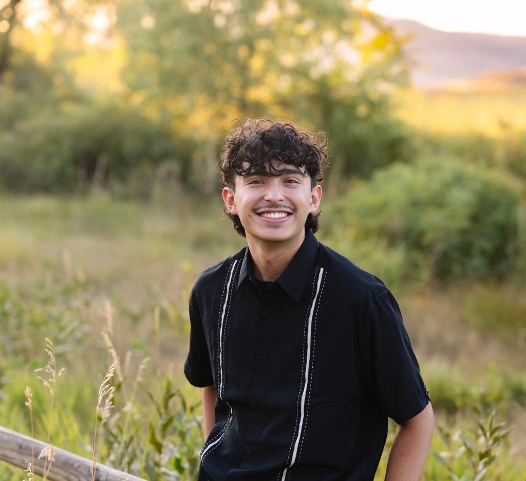 Person in a black shirt with white stripes stands smiling in a field with green grass.