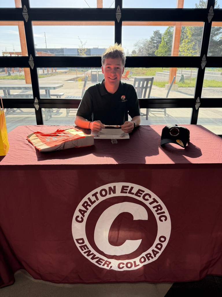 Man signing papers at a table with a maroon tablecloth. Behind him is a window overlooking a picnic area.