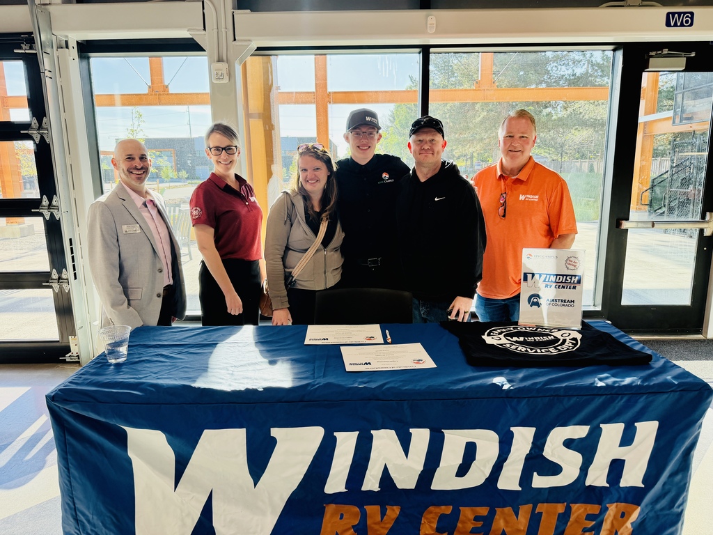 Five individuals stand behind a table with a blue tablecloth. Text on the tablecloth reads "Windish RV Center".
