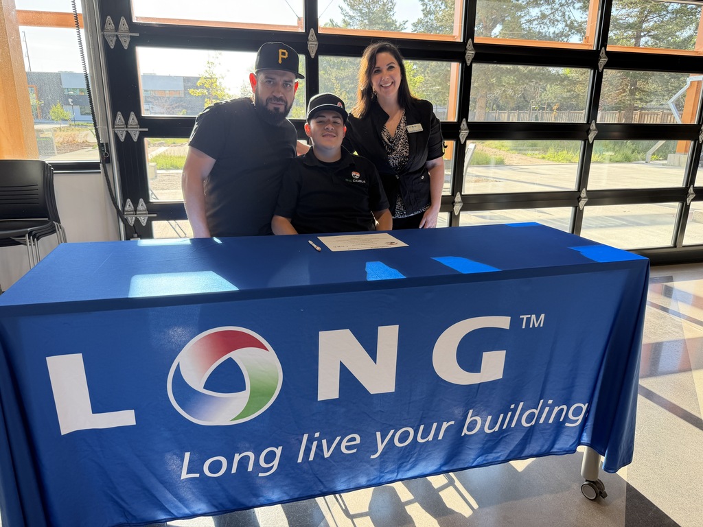 Three people stand behind a table with a blue cloth displaying "LONG" and a logo.