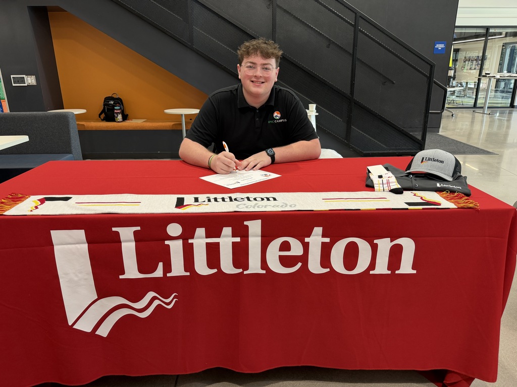 Person sitting at a table with a Littleton banner. Behind, a person is seated on a bench.