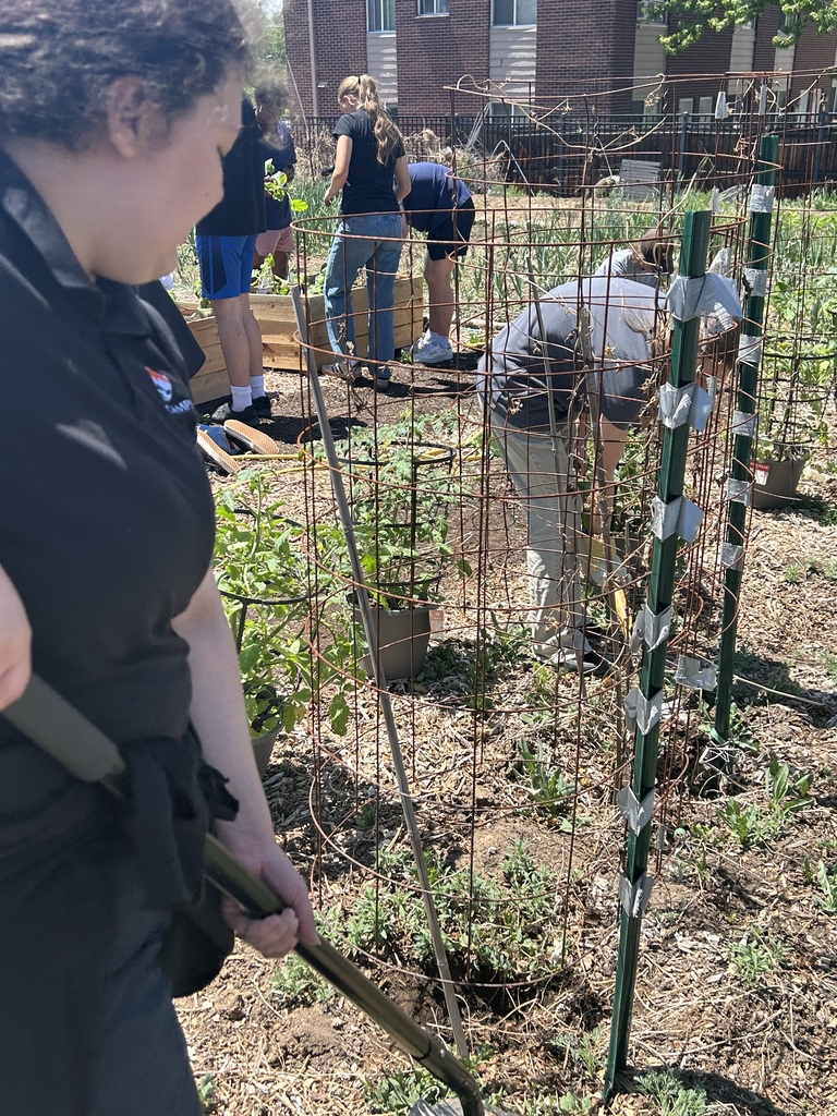 People in a garden, some planting and others bending over. A woman holds a shovel.