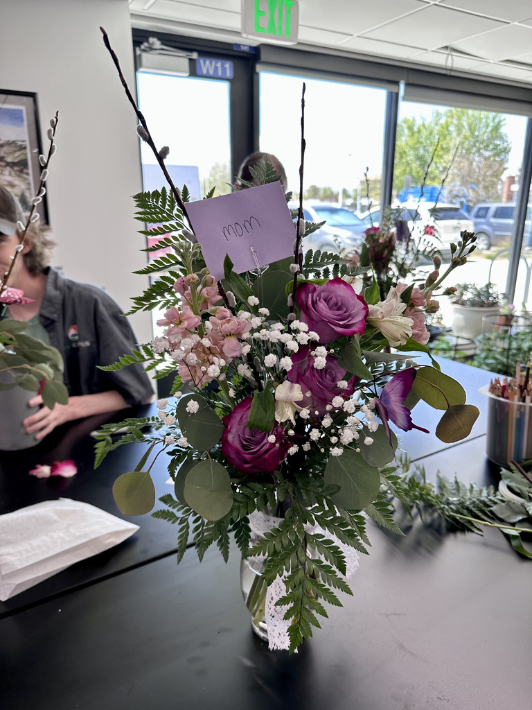 A table displays a floral arrangement in a vase with a note that reads "Mom". The flowers include pink, purple, and white blooms.