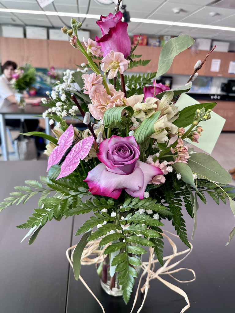Bouquet of pink, white, and peach flowers in a clear vase. Green leaves, pink butterfly, and ribbon.