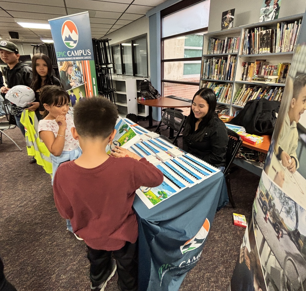 Library event with a table. A boy is looking at something on the table. People are standing and sitting around.