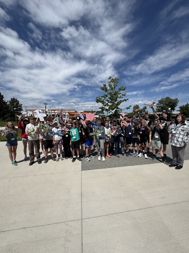 Group of people outdoors, standing in a circle on a concrete surface with a tree in the center.