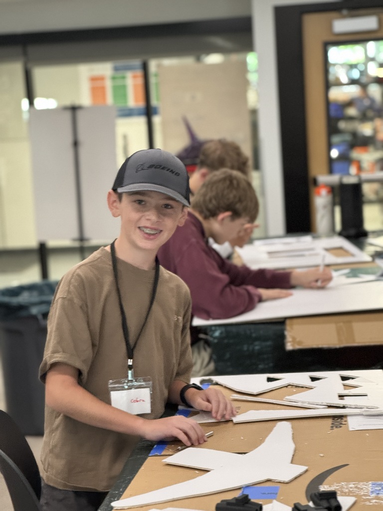 A boy in a cap smiles at the camera. He works on a star-shaped object at a table.