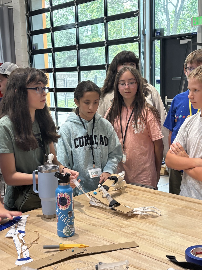 A group of young people are gathered around a wooden table with a project in progress.