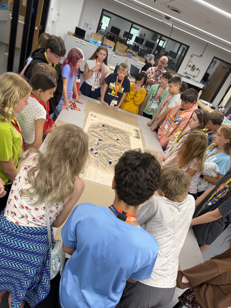 Several children gathered around a table with a large map on it, some wearing lanyards.