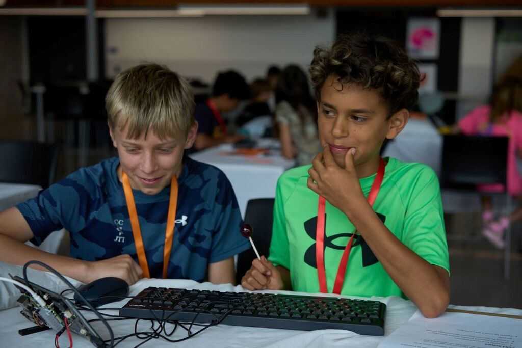 Two kids working on computers in a classroom. One wearing a blue shirt, the other a green shirt.