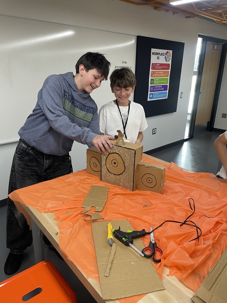 Two children are working on a cardboard project on a table covered with orange plastic.
