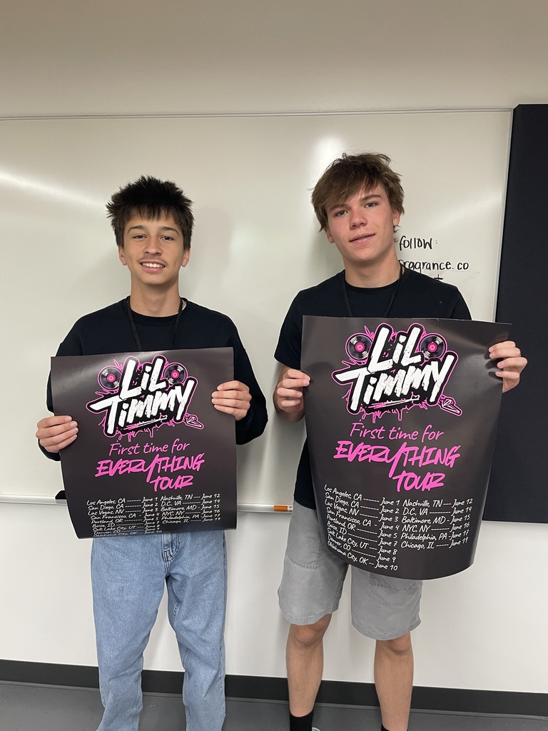 Two boys hold black signs with white and pink text. One reads "Tiny" and the other "Lil Timmy."