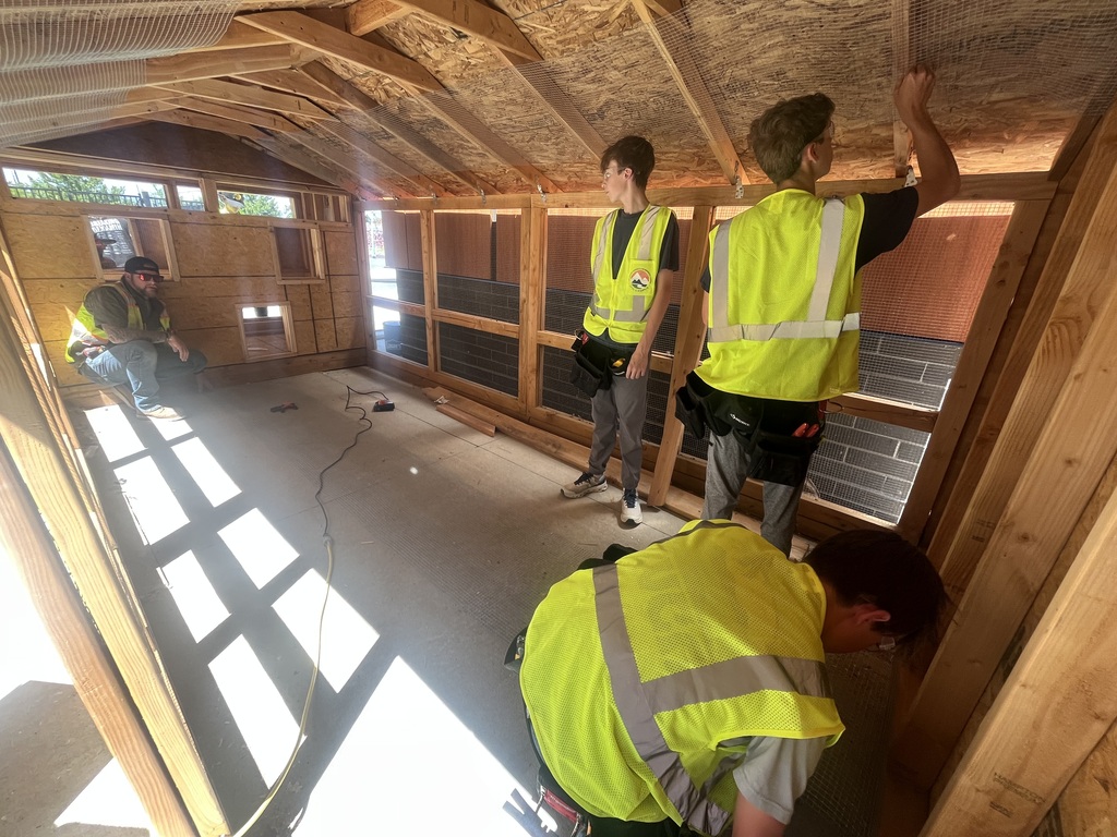 Four people wearing yellow vests work on the interior of a structure with wooden walls and a roof.
