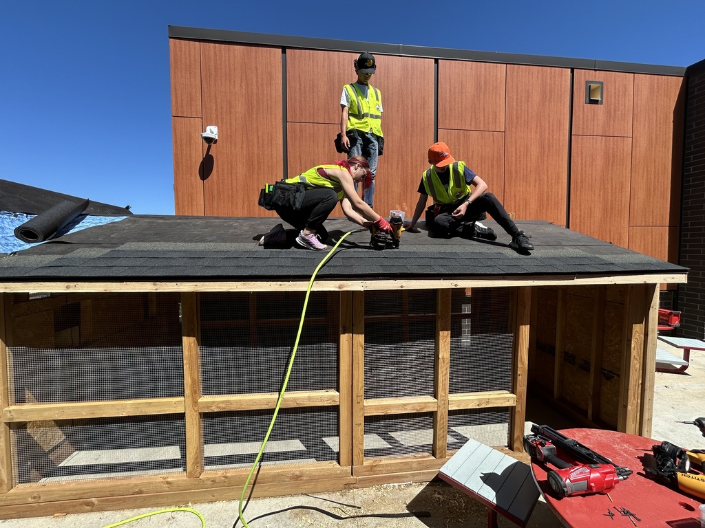 Four people in safety vests work on a wooden structure, two on the roof and two on the ground.