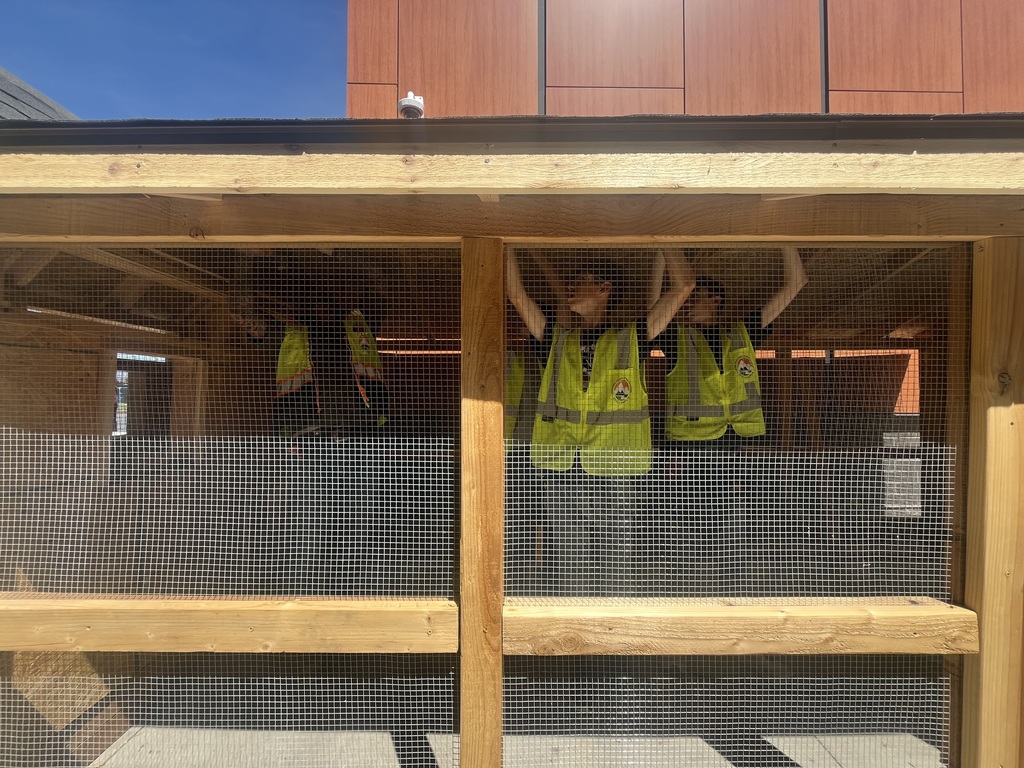 Four people in yellow safety vests stand inside a wooden structure with glass walls, working on the roof.