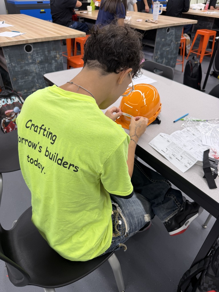 Person in a yellow shirt sitting on a chair at a desk, working with an orange hard hat.