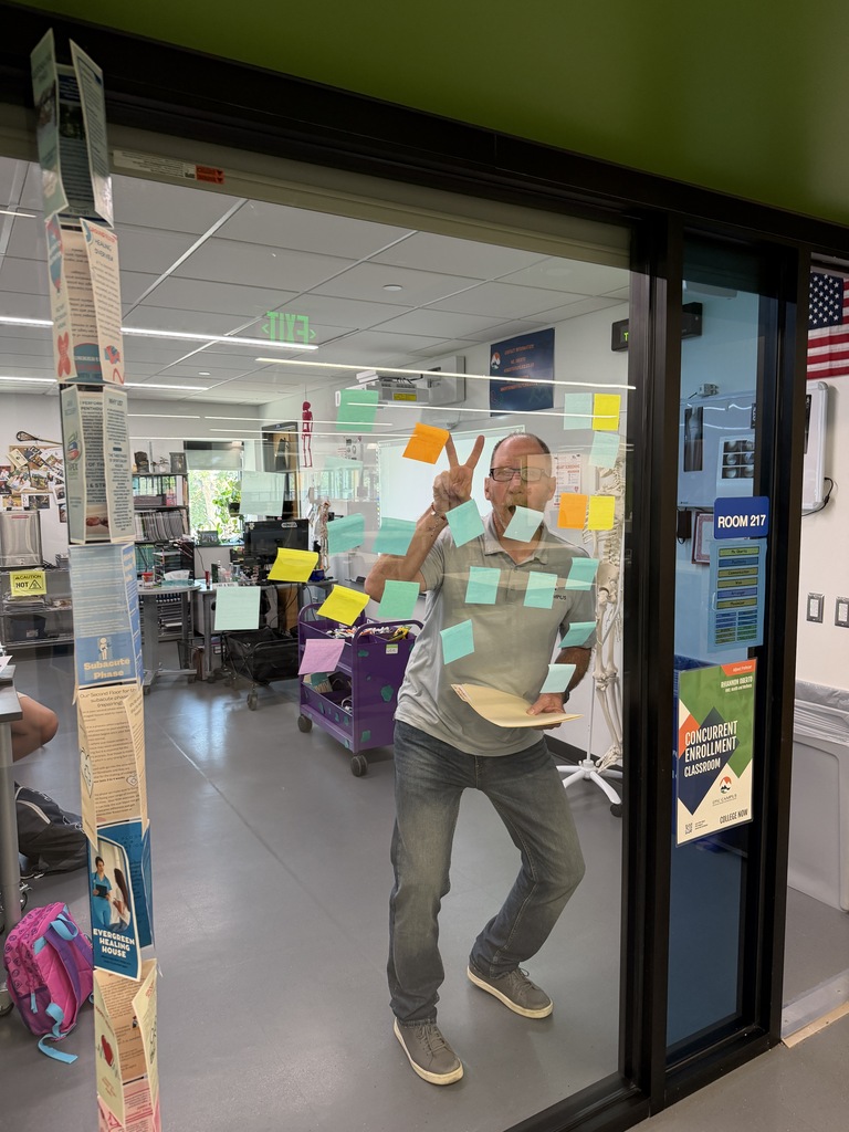 Person with yellow sticky notes stands in front of a glass door. Background includes office space with multiple desks and a flag.