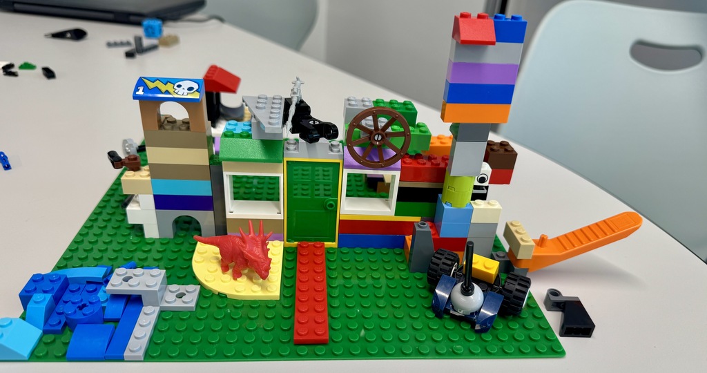 A Lego creation featuring a castle, various buildings, and a wheel, displayed on a white table.