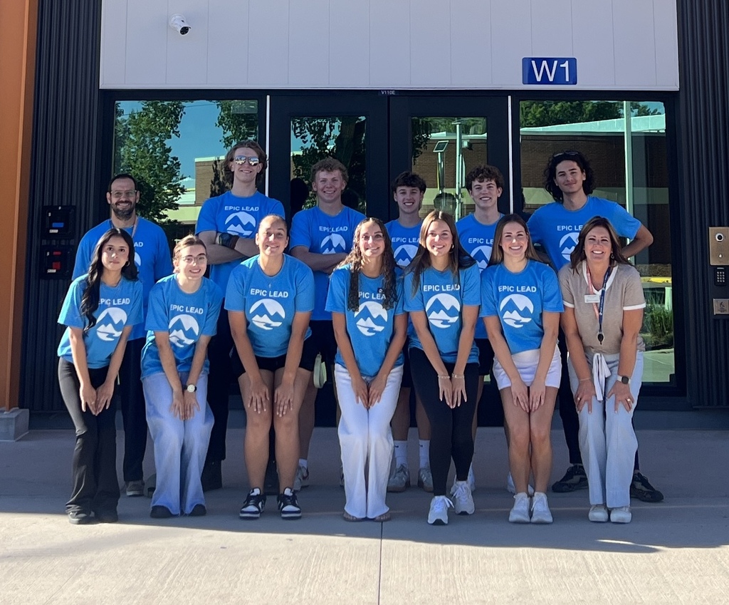 A group of people in blue shirts and white pants, standing in front of a building.