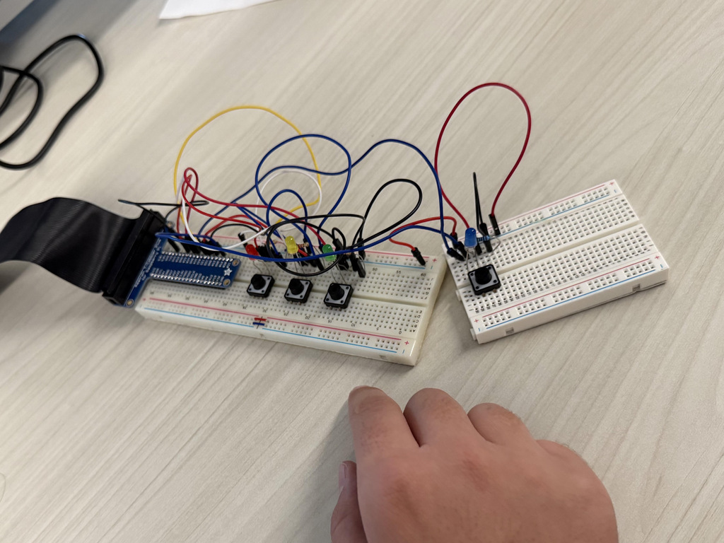 A hand touches a wired circuit board with a microcontroller, buttons, and colored wires on a table.