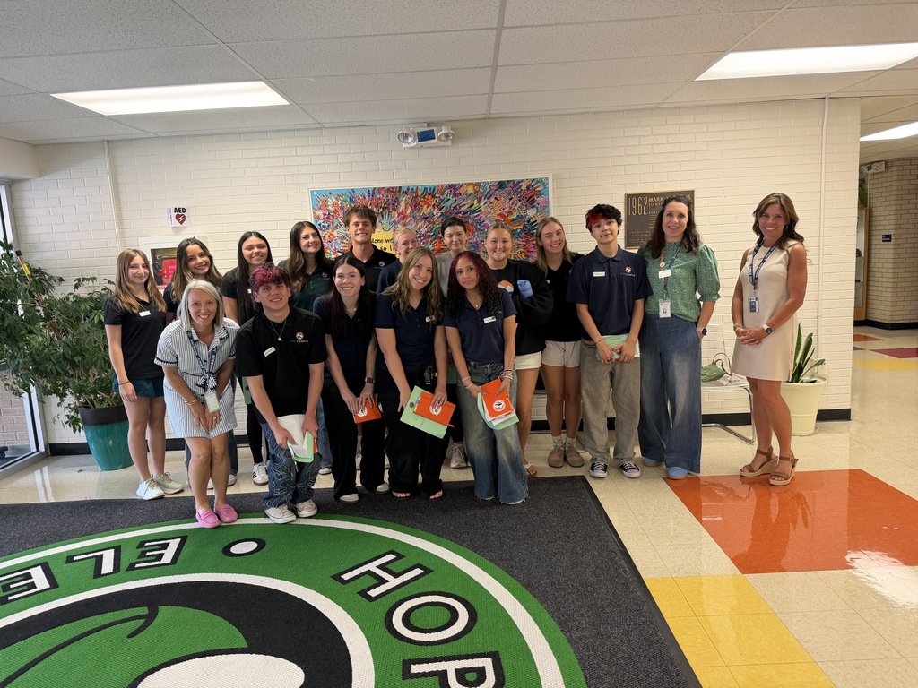 A group of people stand in a hallway with a colorful floor design, wearing matching uniforms.
