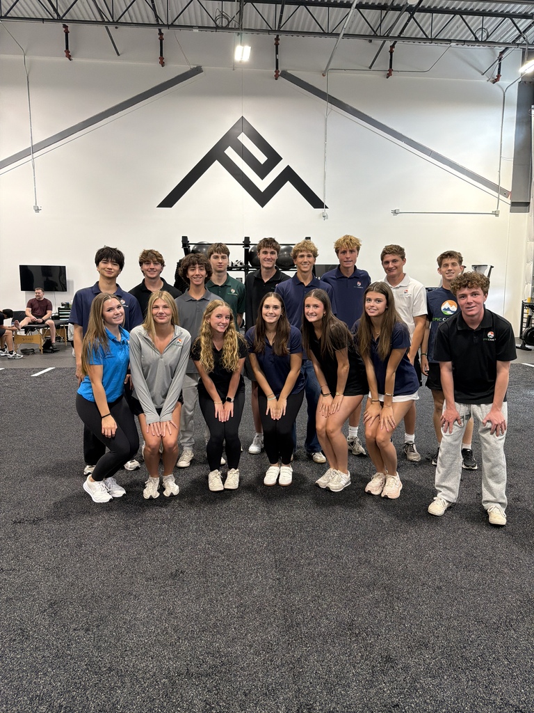 Group of people in matching uniforms, posing for a photo in a gym with a large triangle design on the wall.