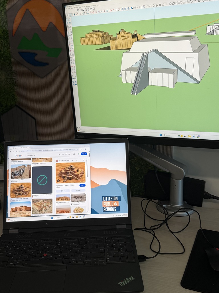 A laptop displays a 3D architectural model on a large monitor. The room features a green wall with a circular logo.