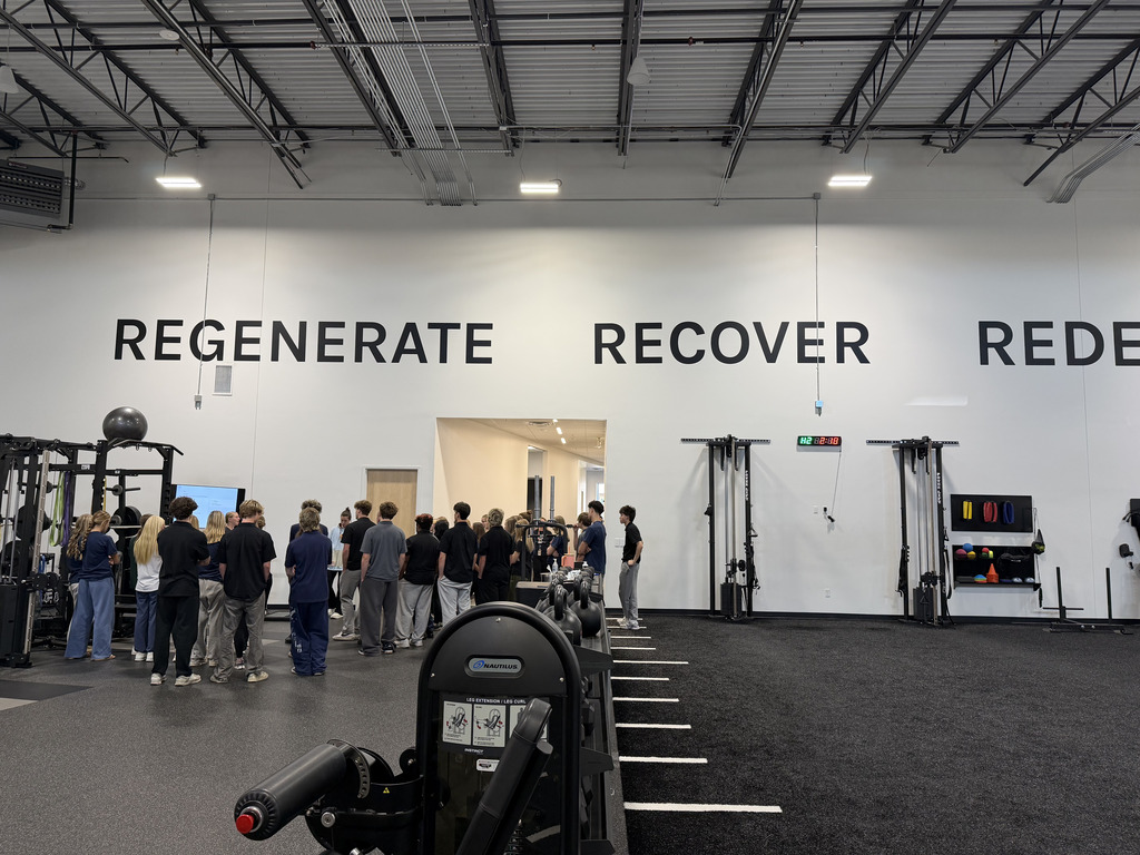 People stand in a gym, with large white walls and the words REGENERATE, RECOVER, and REDEEM.