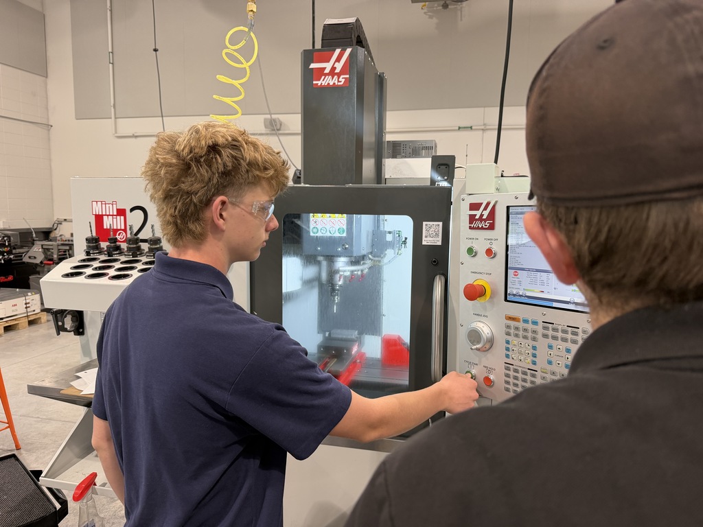 Two people examine a large machine in a factory. One presses buttons on a control panel.