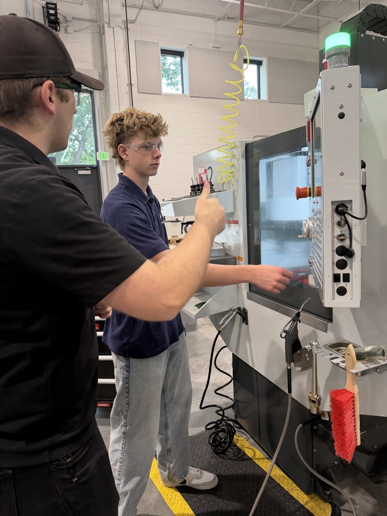 Two people in a room with a large machine. One person points to a screen on the machine.