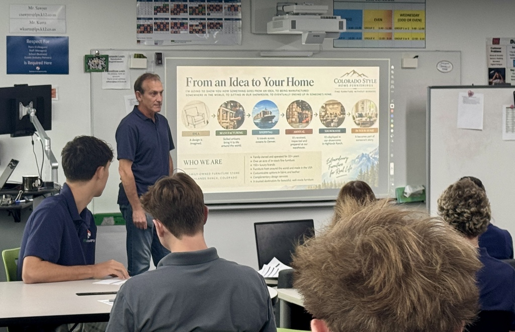 A classroom with a teacher in front of a projector screen explaining something to seated students.