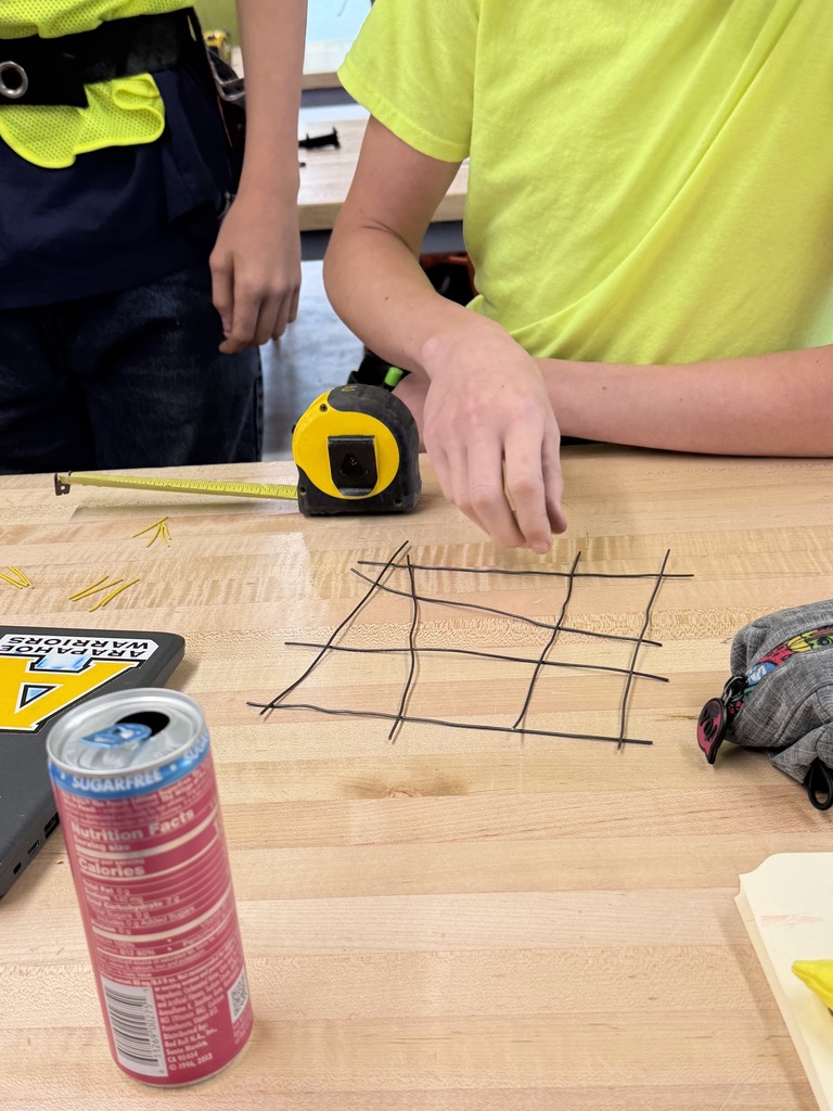 Two people in yellow shirts sitting at a table, working on a project with a grid and tools.