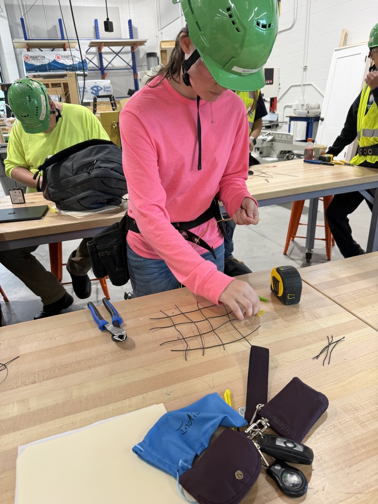 A group of people wearing hard hats and safety vests work on a project at tables.