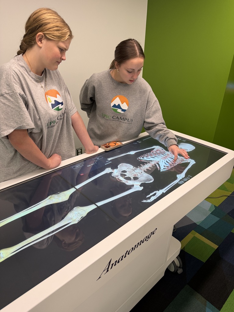 Two individuals examine a large skeleton on a display table. One person stands at the front, the other behind.