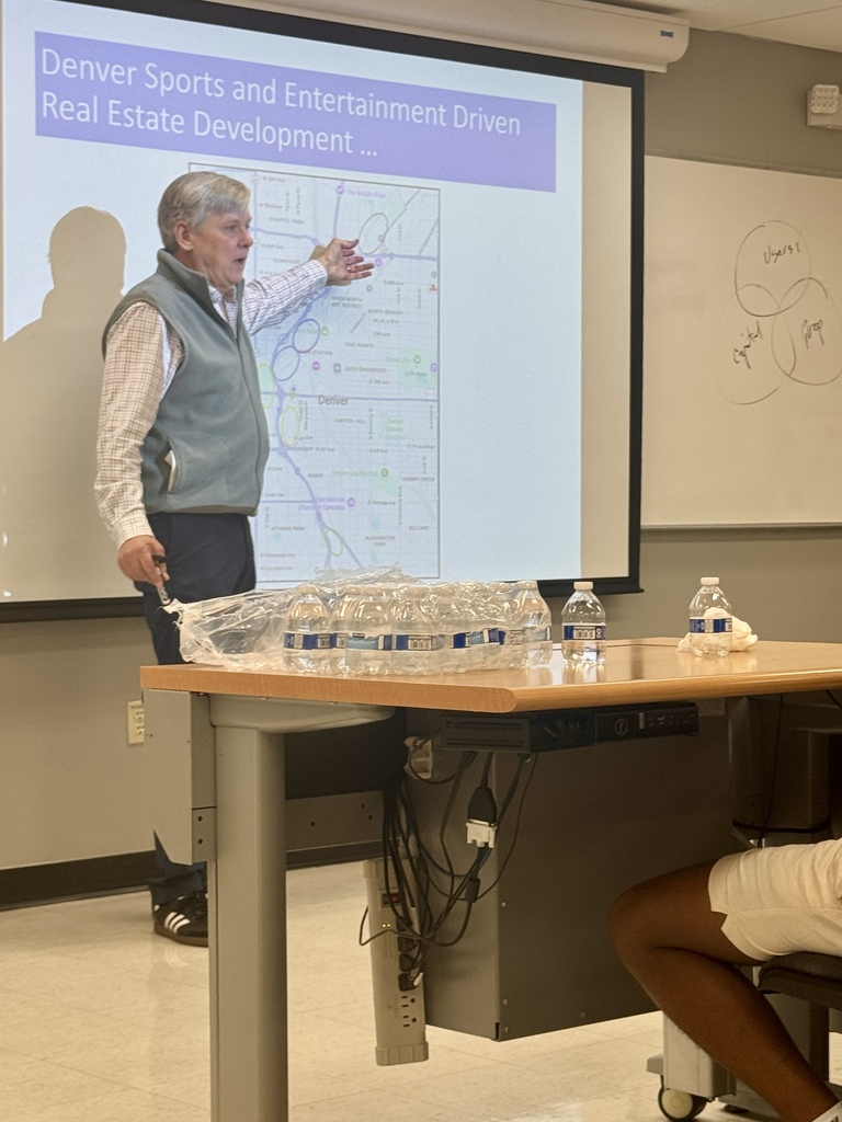A man points at a map on a projector screen. A student sits at a table.