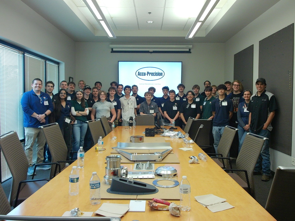 Group of people standing in a meeting room with a long table, chairs, and a projector screen.
