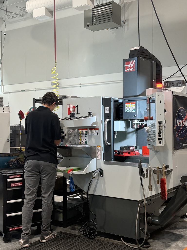 A man wearing a black shirt and gray pants operates a large machine in a factory.