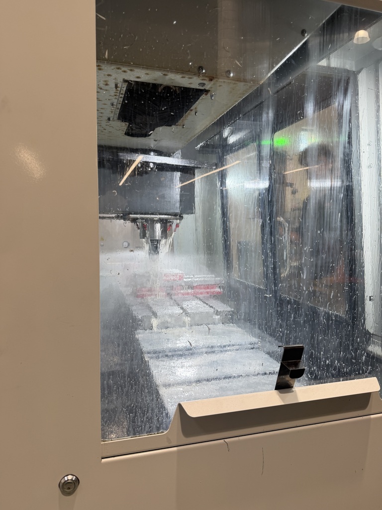 A glass door showing a factory with a machine cutting materials. The machine is surrounded by metal structures.