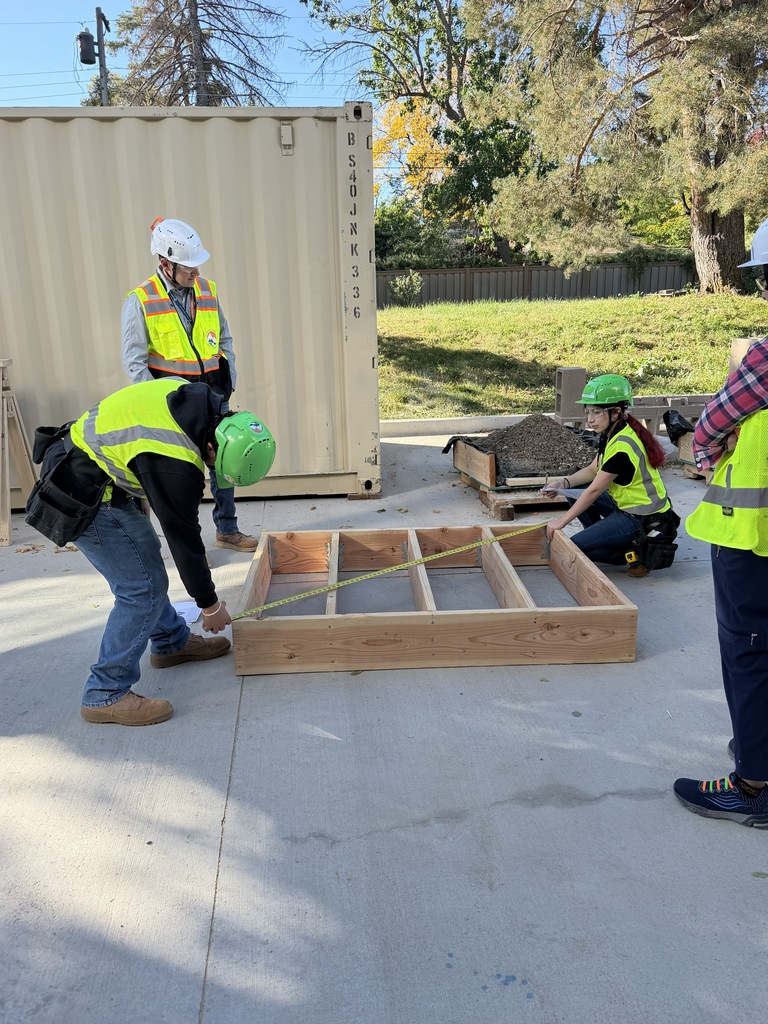 A group of people in high-visibility gear are working on a wooden structure in an outdoor area.