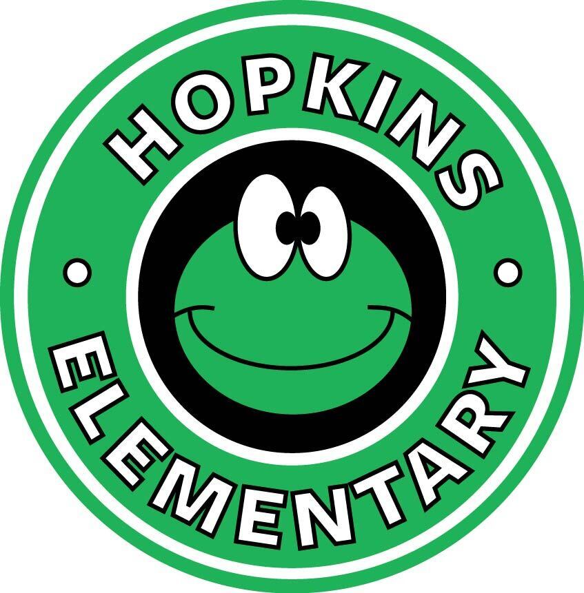 Circular logo for Hopkins Elementary with a green outer border containing the white text "HOPKINS ELEMENTARY" separated by two small circles. The center features a black circle with a cartoon green frog head inside, showing large white googly eyes and a wide, friendly smile.