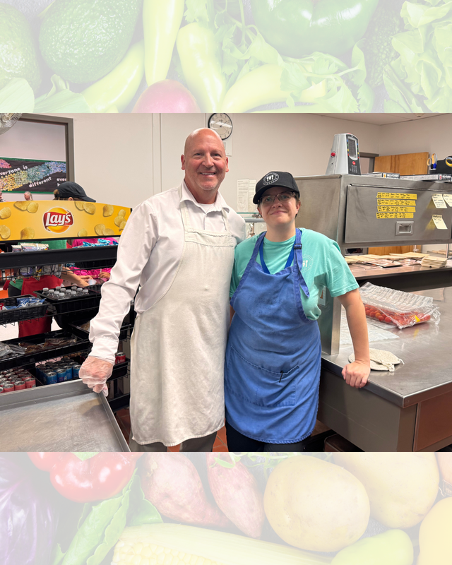 Two school nutrition staff members in aprons smiling together next to a potato chip rack and serving station.