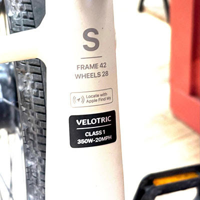 Close-up of a white Velotric bike frame showing size S, 42 frame, 28 wheels, Apple Find My logo, and Class 1 350W-20MPH label.