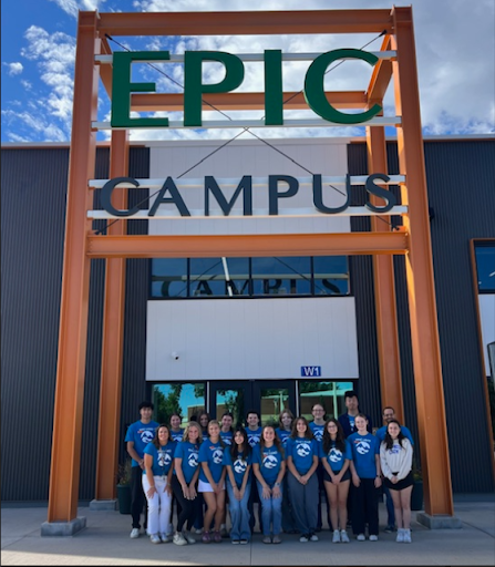 A group of people wearing matching blue shirts are standing outside of a large building with "EPIC CAMPUS" written in big letters on the front. They are posing for a group photo.