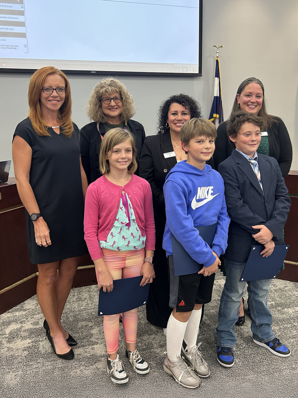 Three Gaskill Elementary students stand with the Board of Education in the LPS Boardroom. They hold their Student Spotlight certificates.