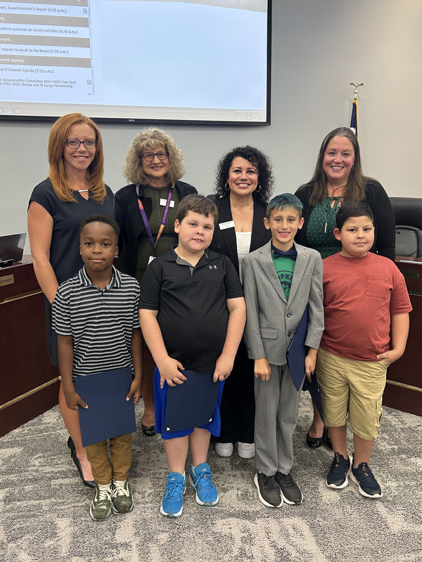Four students from Hopkins Elementary stand with the Board of Education in the LPS Boardroom. They hold their Student Spotlight certificates.