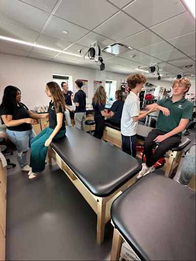 Students work in pairs in a sports medicine lab, practicing physical assessments and treatments on one another while sitting on black treatment tables.